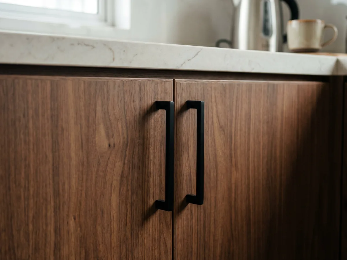 Walnut kitchen cabinet detail with matte black handles and marble countertop